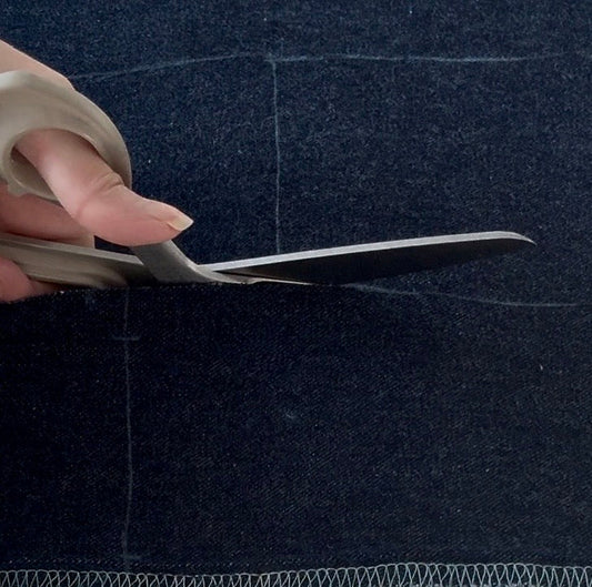 Close-up of cutting reworked denim with visible chalk pattern lines and raw edge stitching in the Yan Neo studio